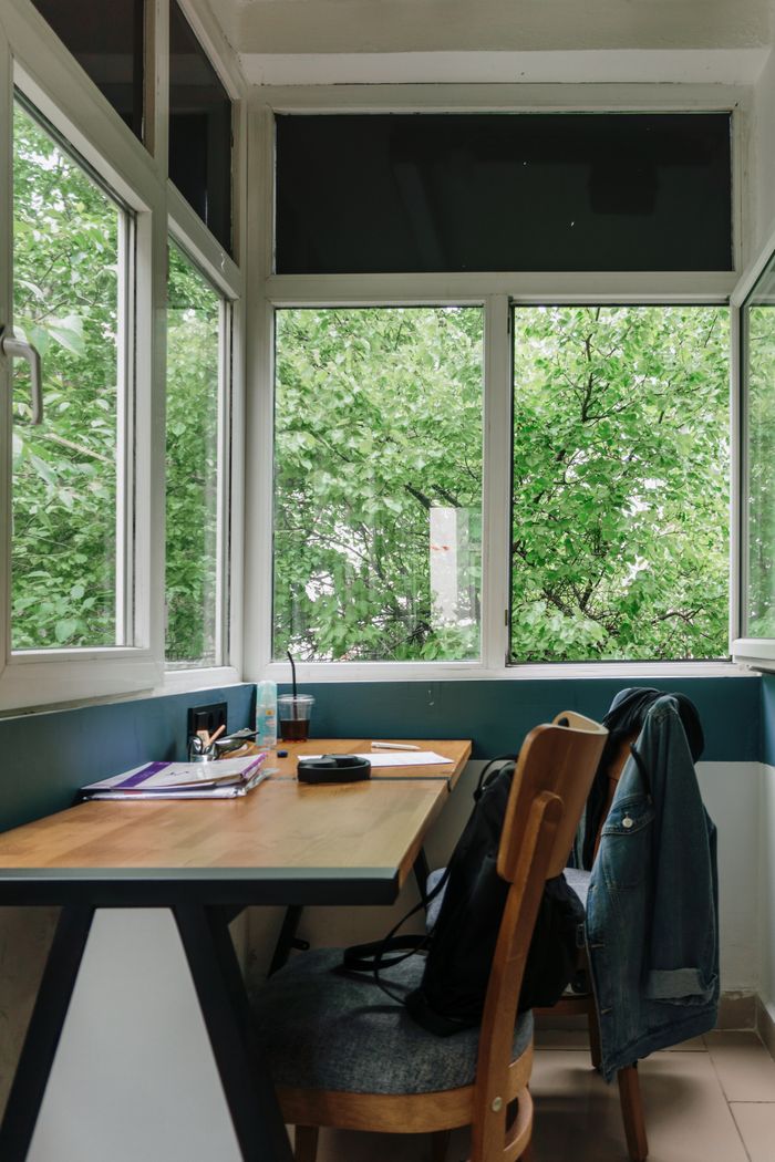 A peaceful workspace with large windows offering a view of lush greenery, featuring a desk, chair, and casual attire.
